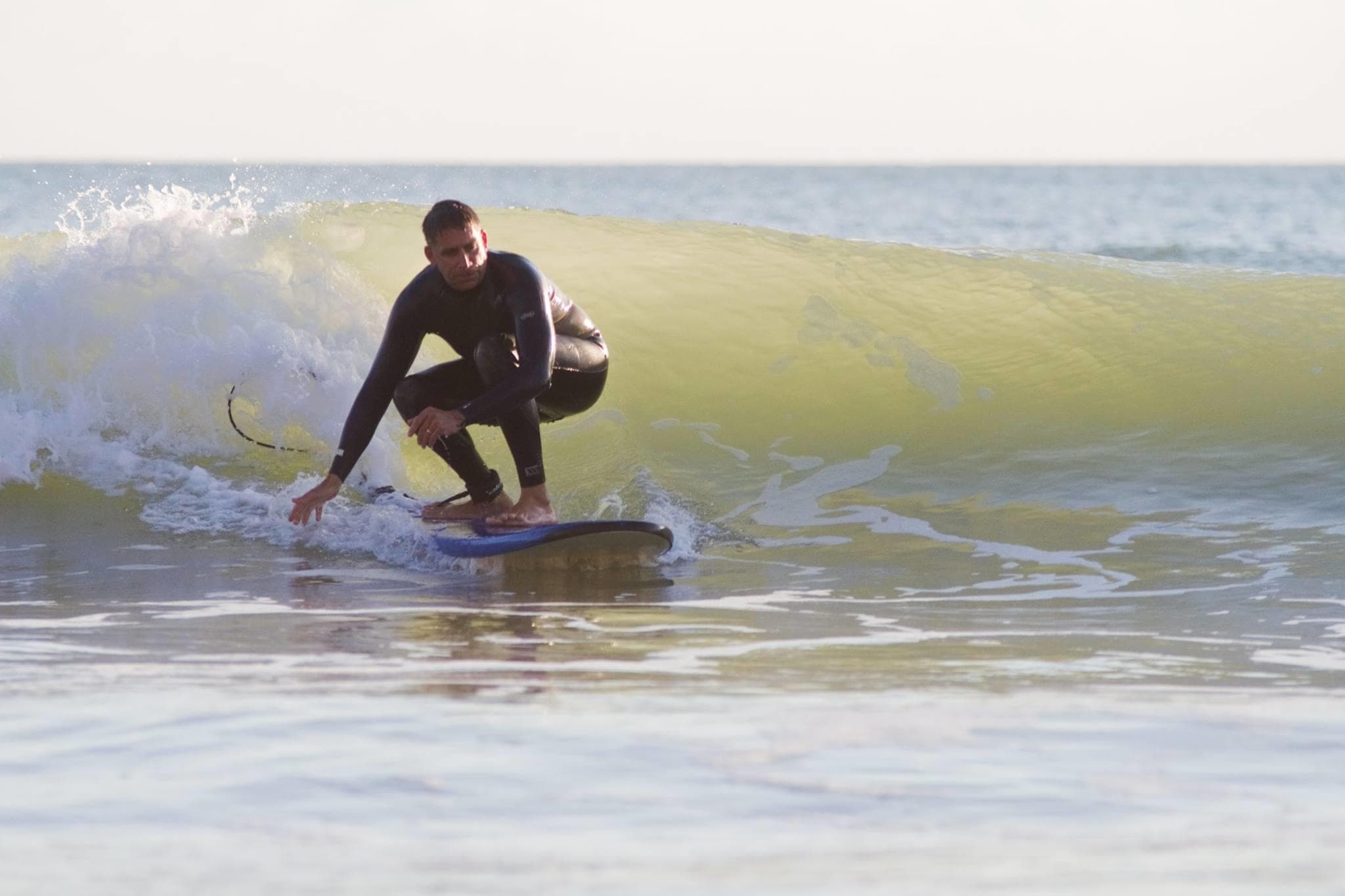 Surfer carving green wave close to shore in sunny surf