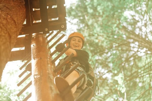 Participant climbing wooden platform on shaded treetop course