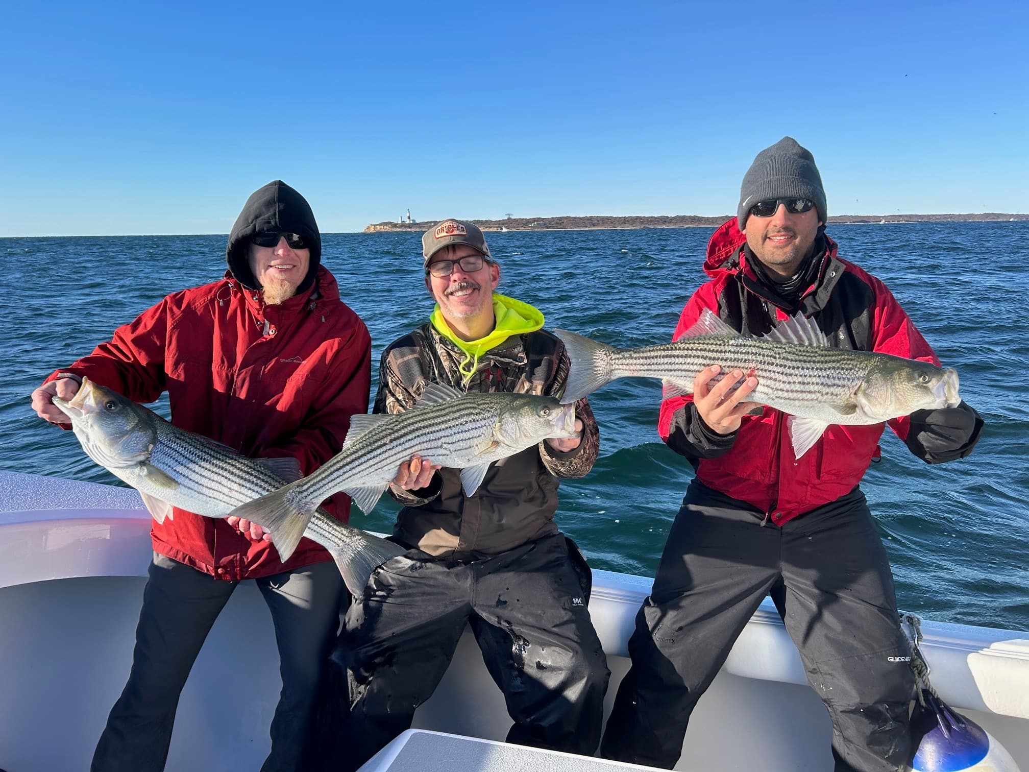Three anglers proudly holding striped bass aboard sportboat