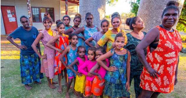 Group of Indigenous women and children posing on grassy community grounds