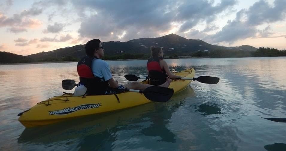 Two kayakers paddling at sunset over calm coastal waters