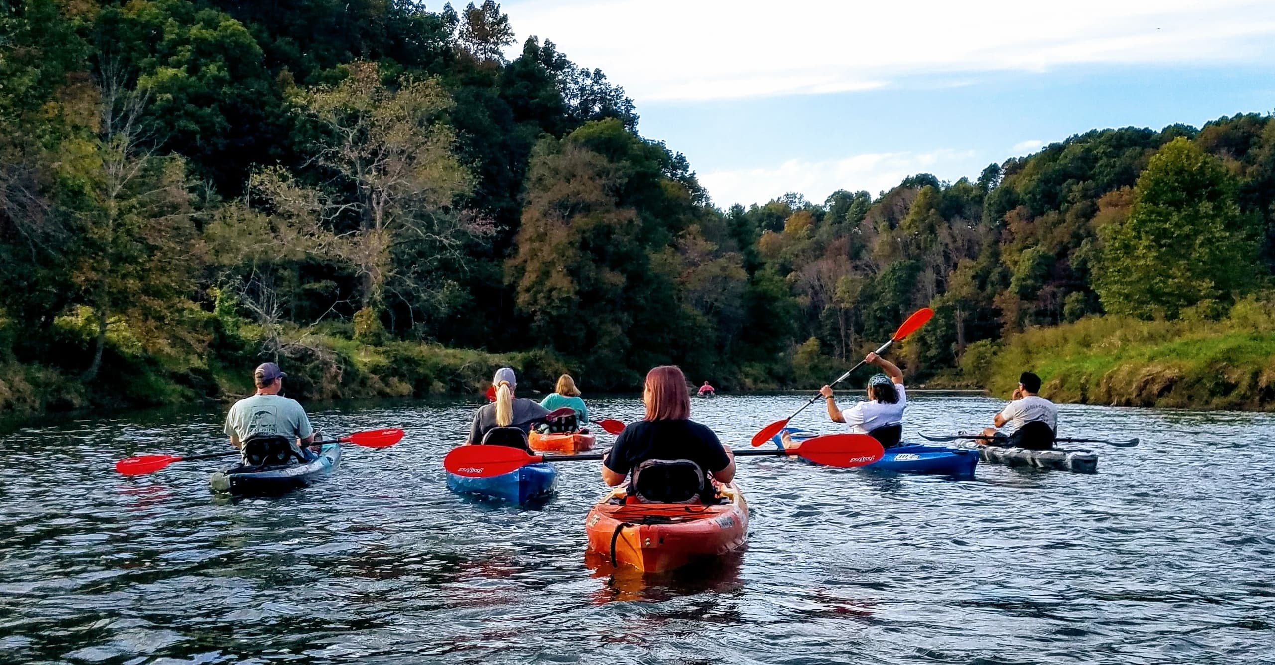 Group of kayakers paddling downstream through scenic river