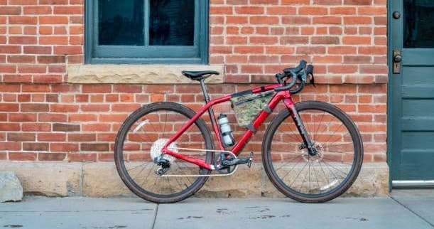 Red gravel bike leaning against brick wall in urban alley