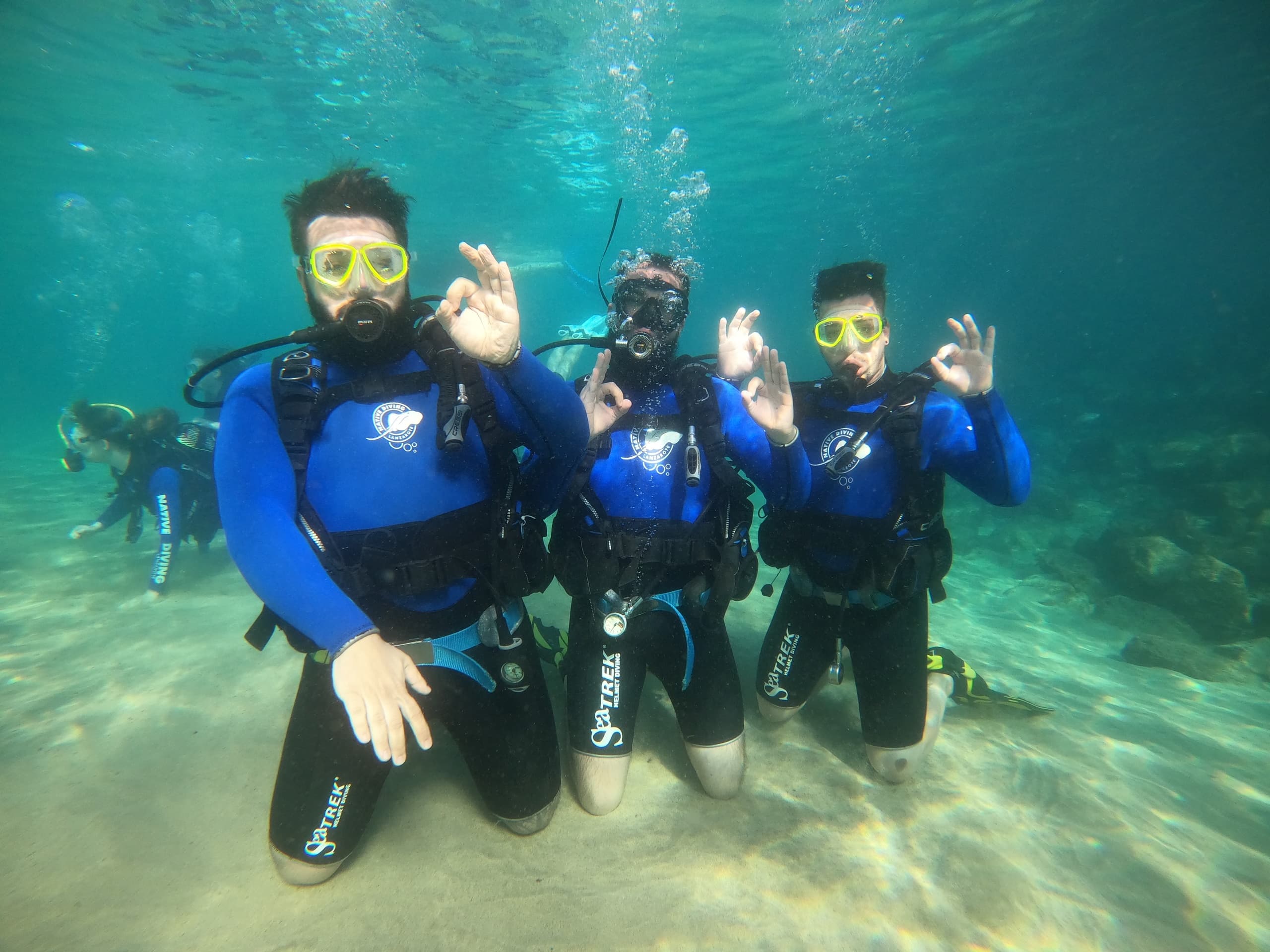Three scuba students kneeling on sandy bottom signaling OK underwater
