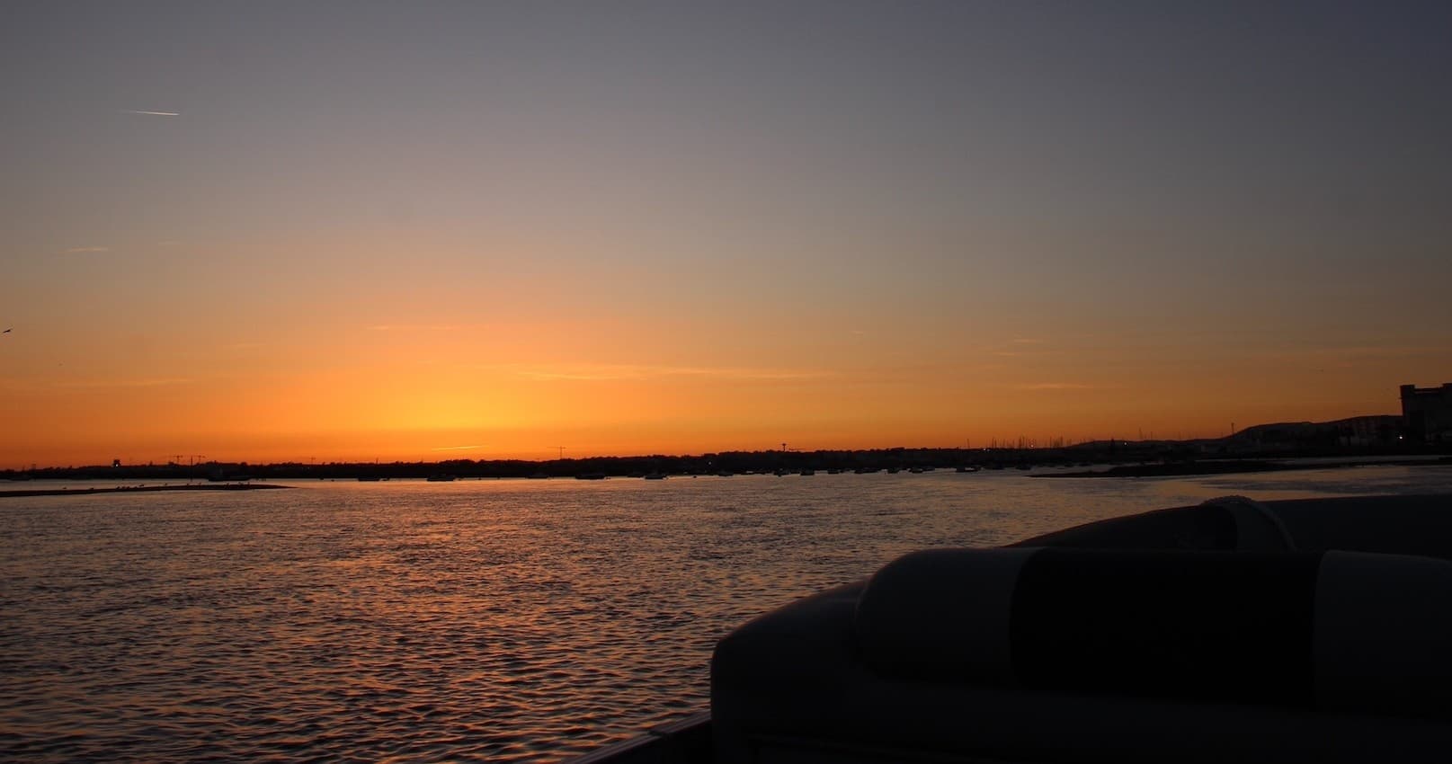 Sunset over calm sea with silhouetted boat on Algarve horizon