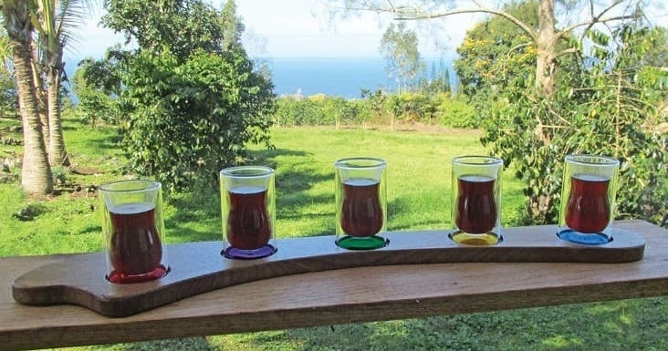Coffee tasting flight on wooden paddle with ocean view backdrop