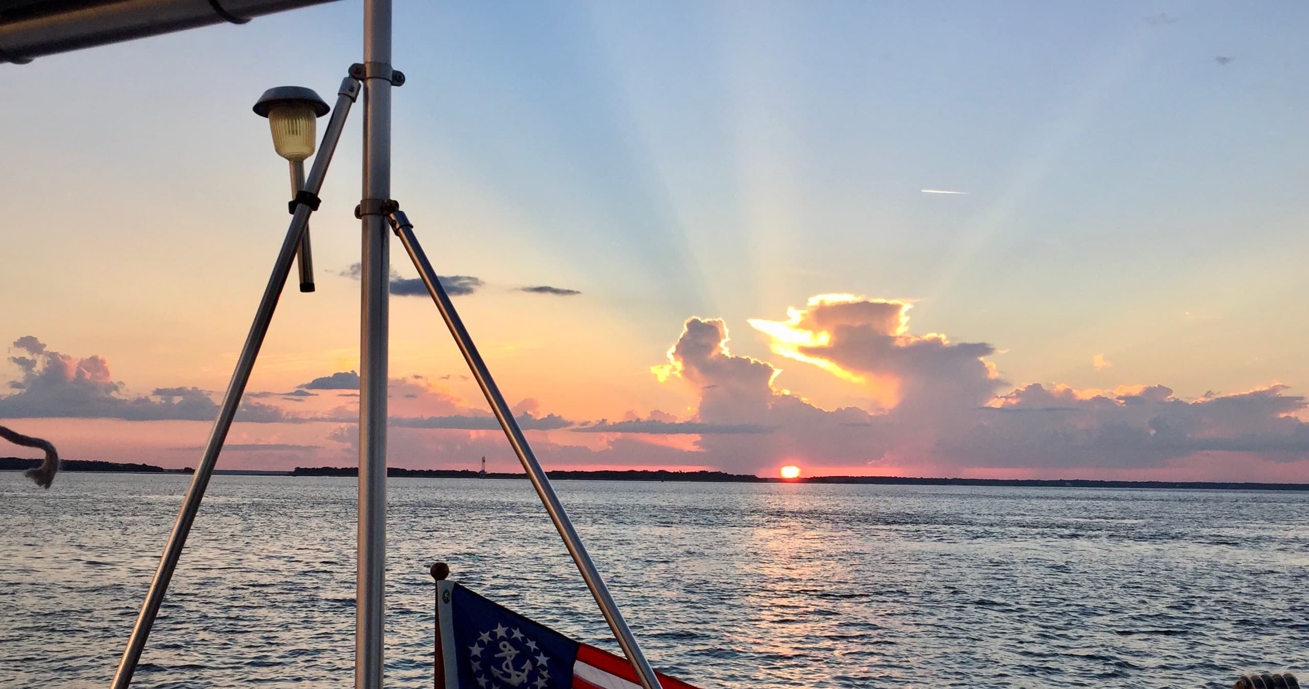 Sunrise over calm water seen from sailboat stern with flag