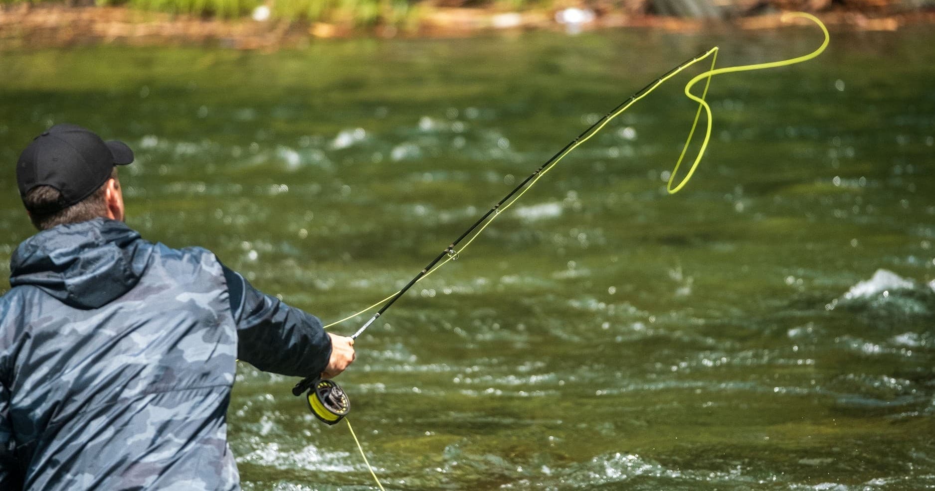 Fly fisher casting a line across rushing river, dynamic angling action