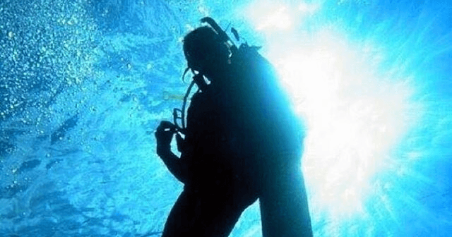 Scuba diver silhouetted against bright sunlit ocean surface