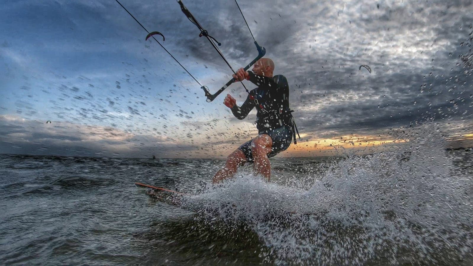 Kiteboarder carving through spray on open water at sunset