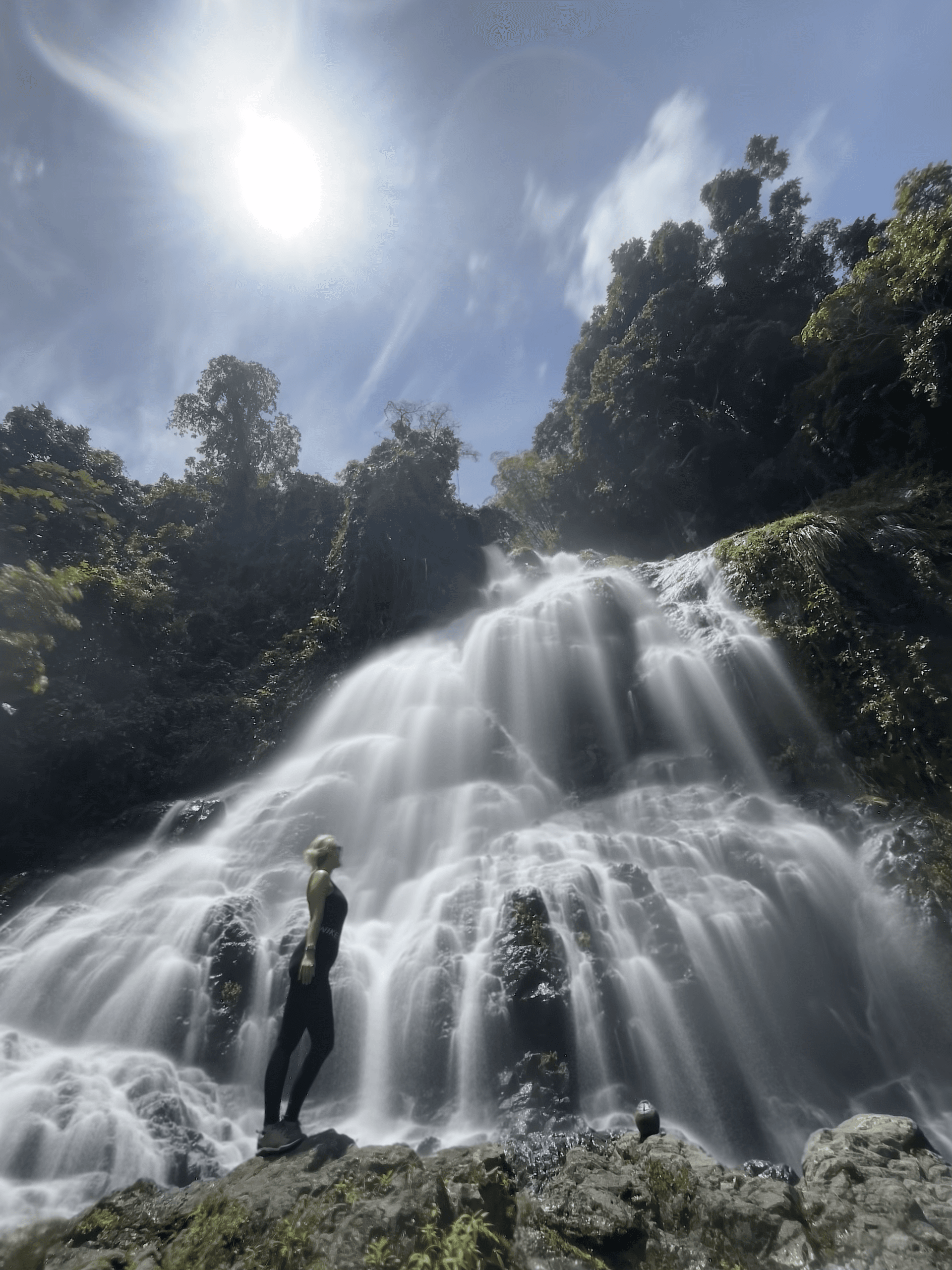 Hiker standing before multi-tier waterfall under bright sun