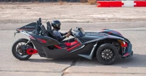 Black Slingshot side profile with driver on open road parking area