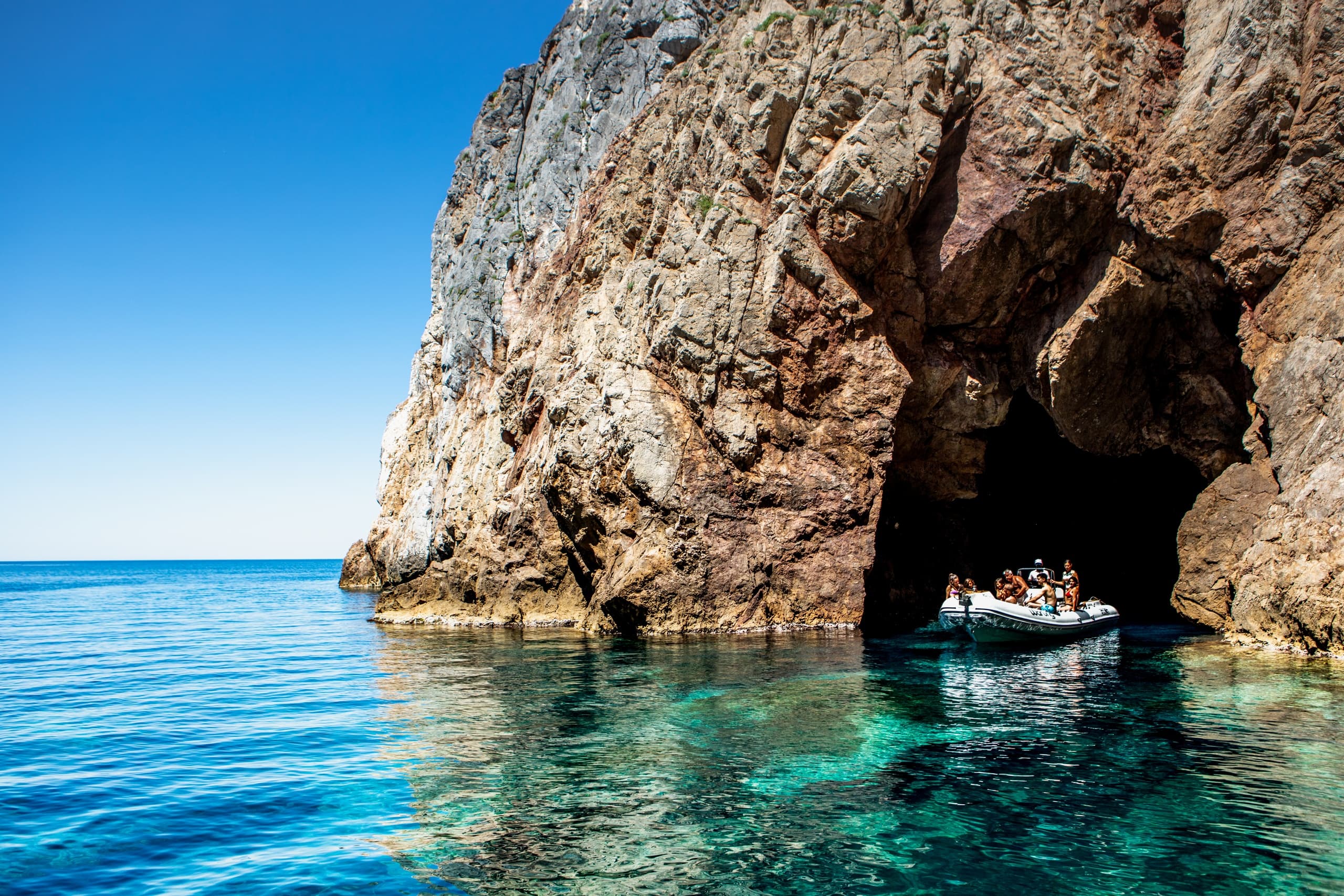 Tour boat entering sea cave at rugged coastal cliffs