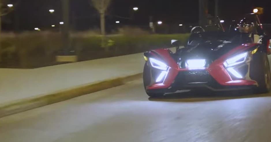 Slingshot driving at night on city street with headlights