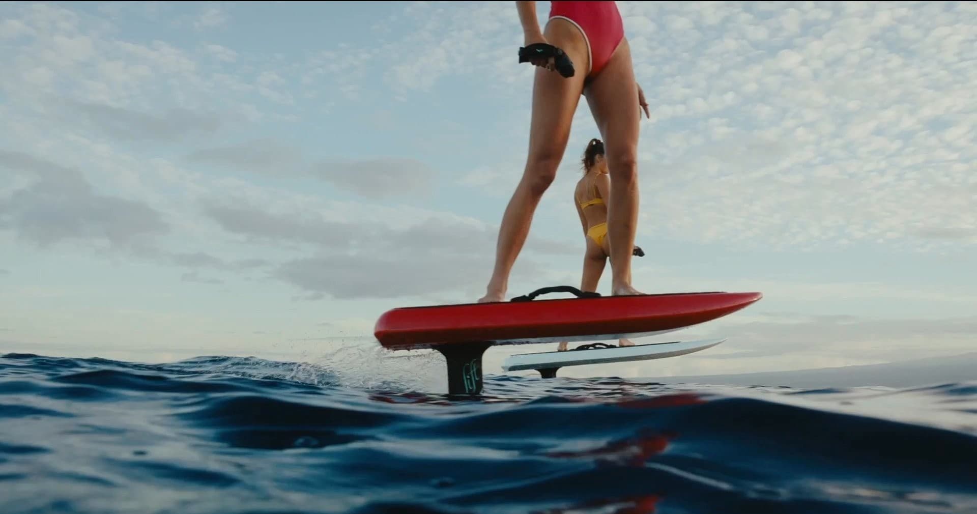 Close-up hydrofoil rider balancing on a red foil board over open water