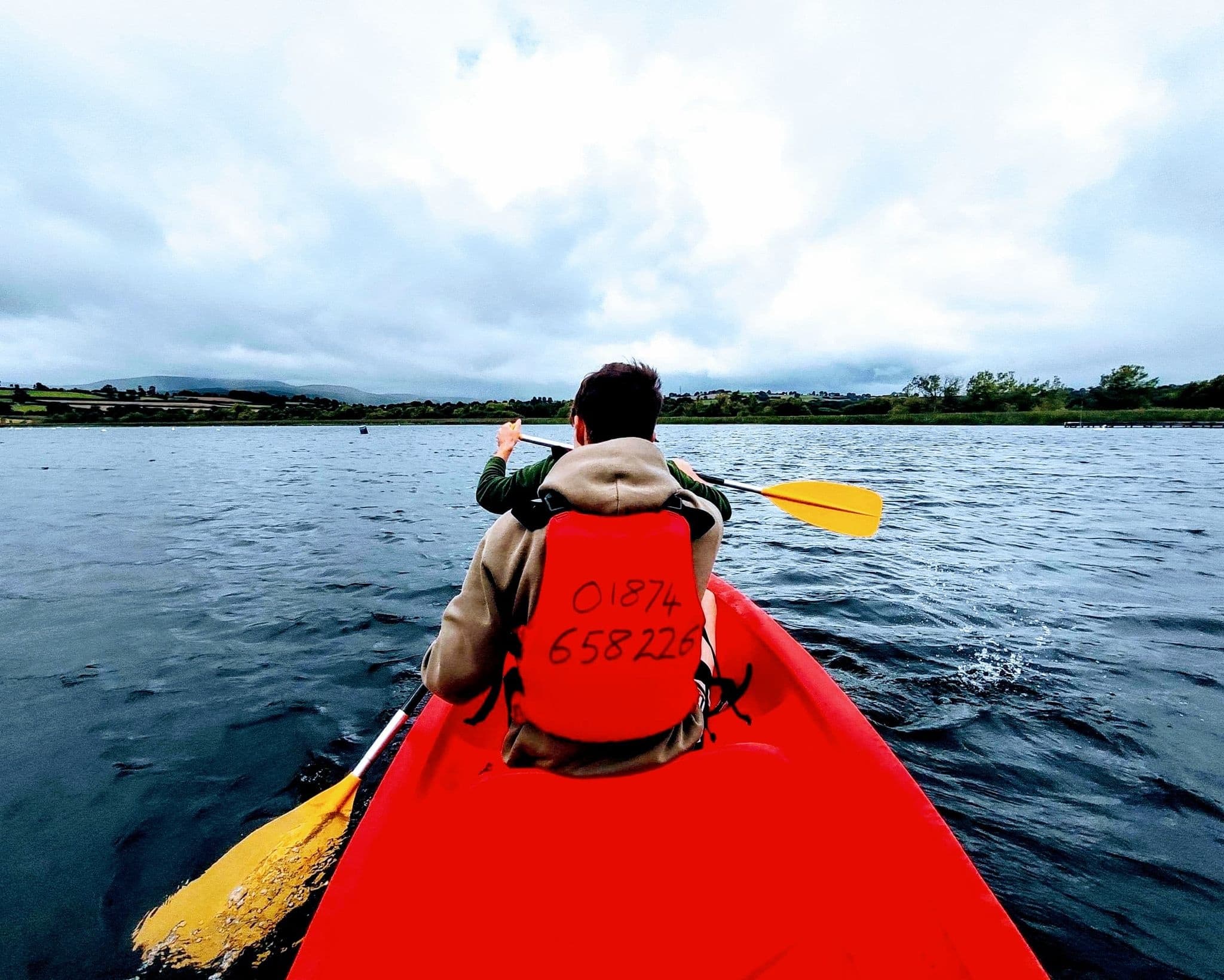 Paddler kayaking from stern view across open water on lake