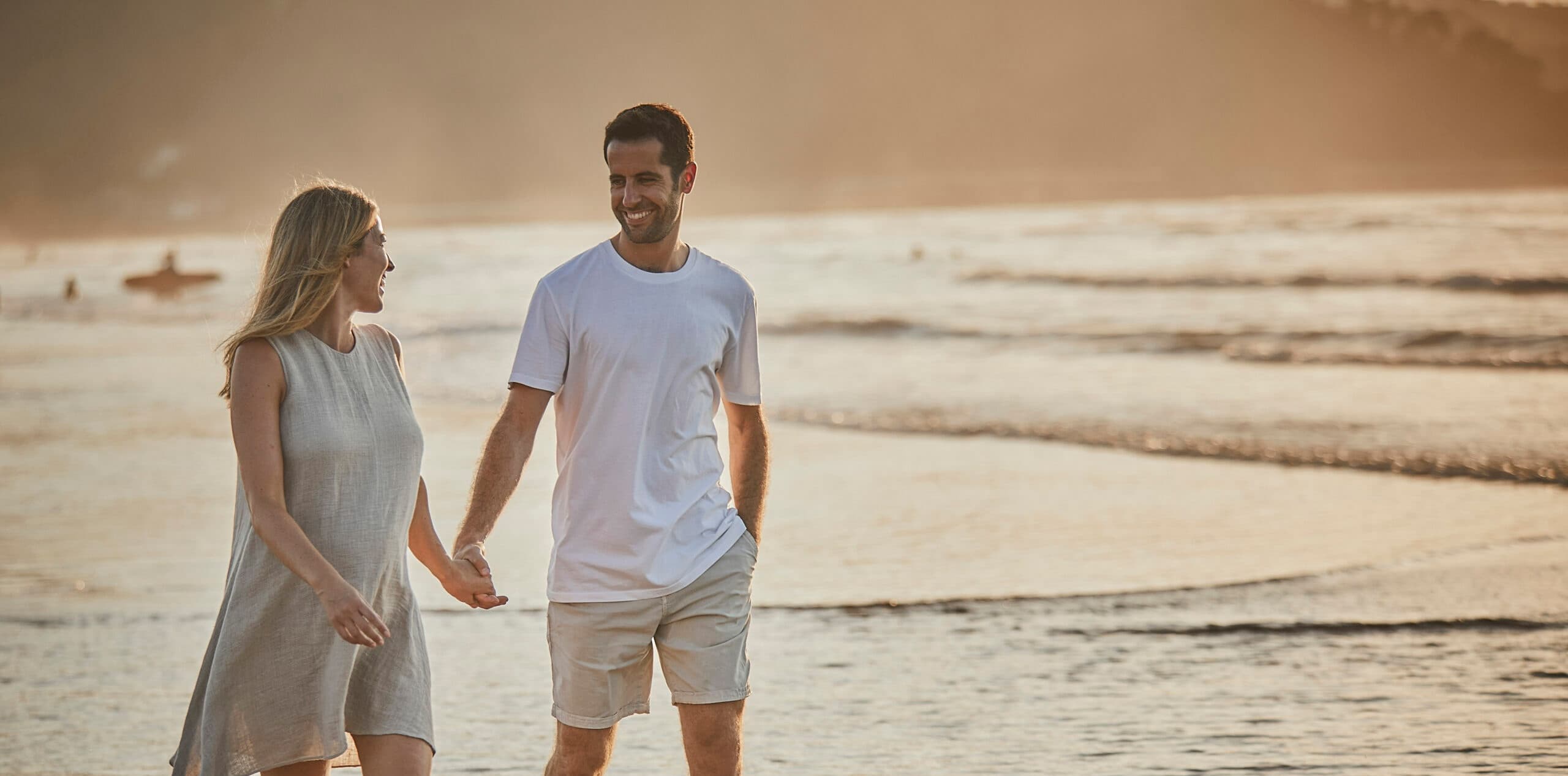 Couple walking hand in hand on sandy beach at golden hour
