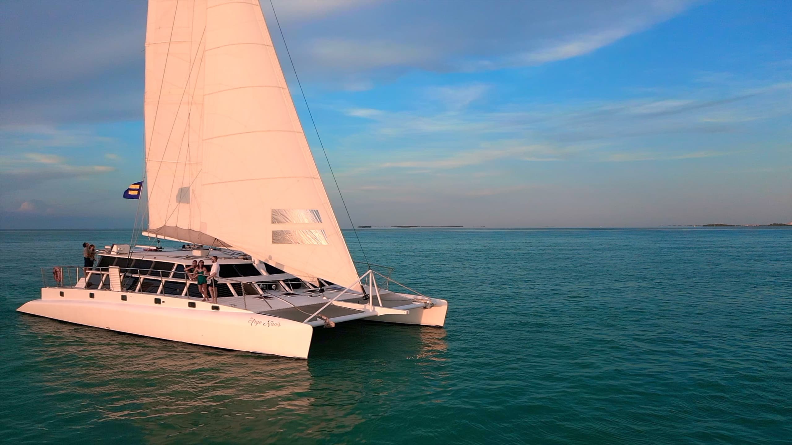 Luxury catamaran sailing on calm sea under blue sky at sunset