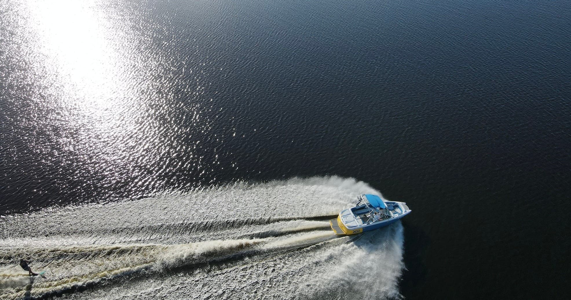 Aerial powerboat cutting wake across open bay at sunset