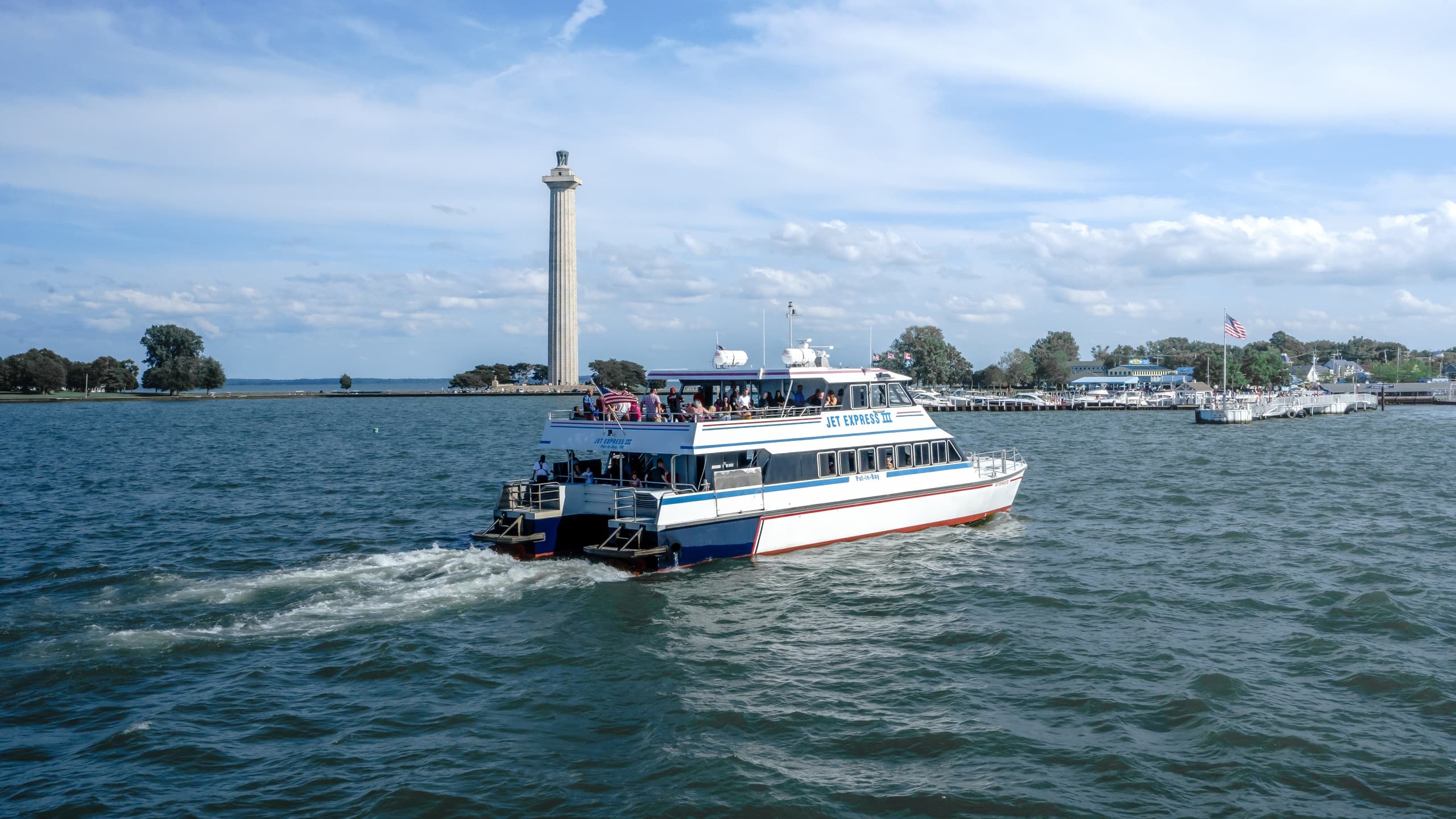 Ferry cutting through water past a shoreline lighthouse