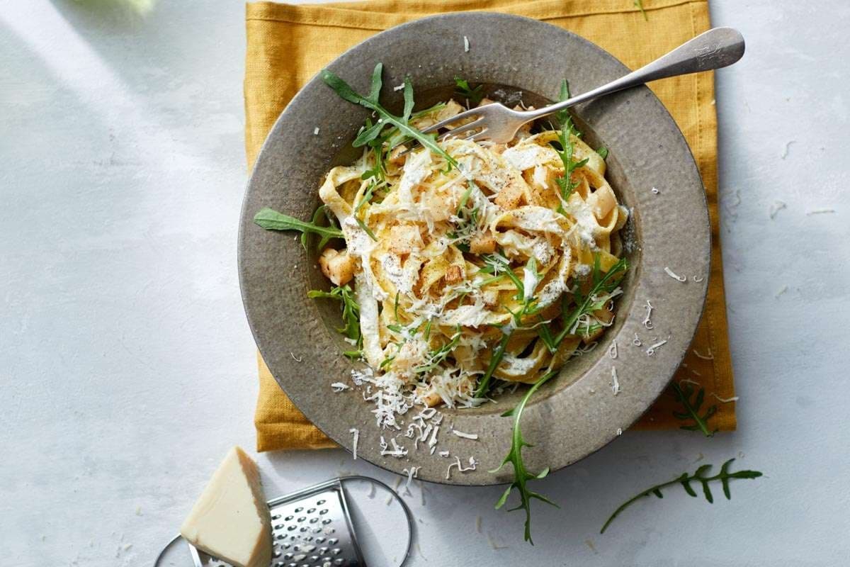 Creamy vegan pasta bowl garnished with herbs in studio kitchen