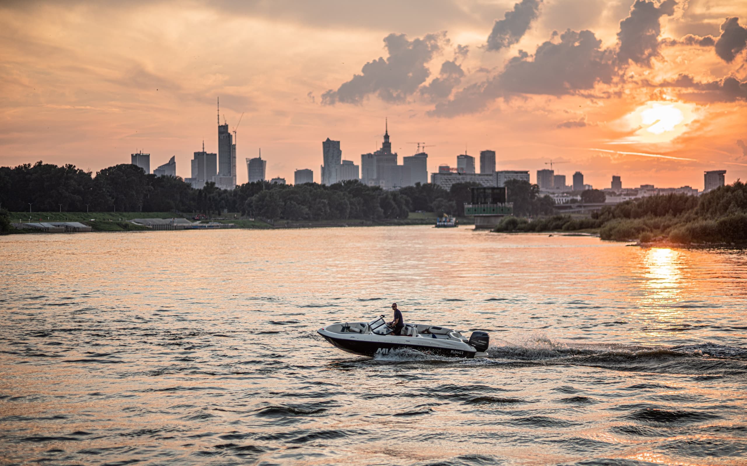 Small motorboat silhouetted against Warsaw skyline at sunset