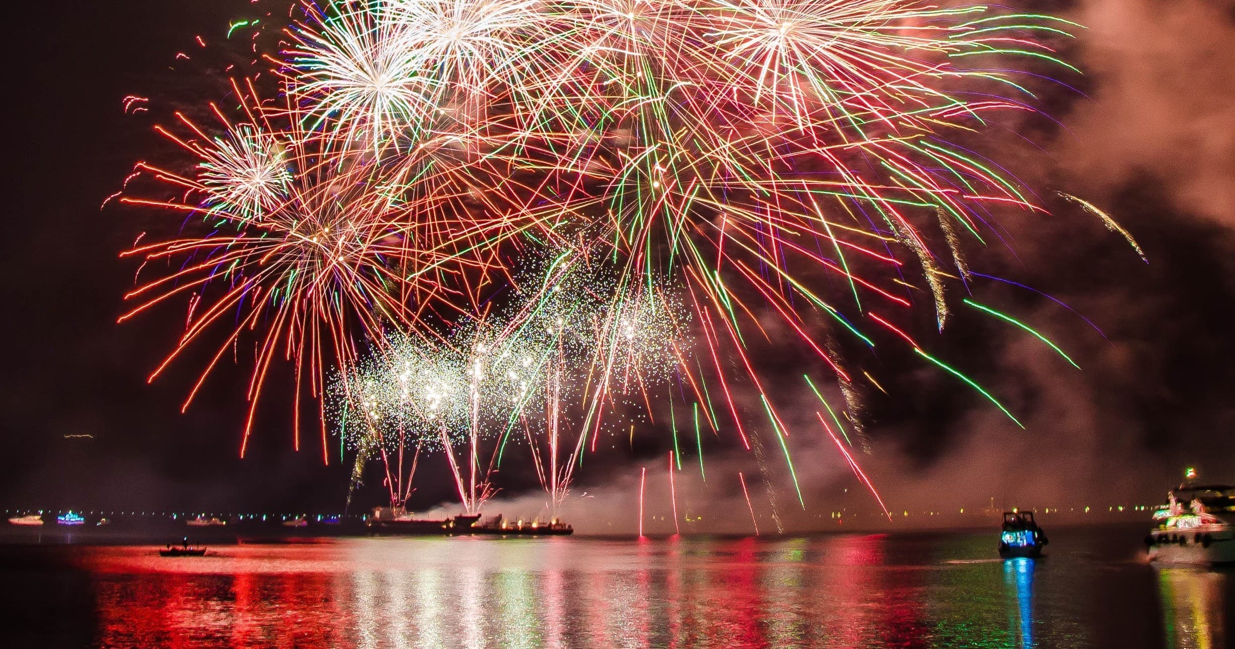 Fireworks display over harbor at night with reflections on water