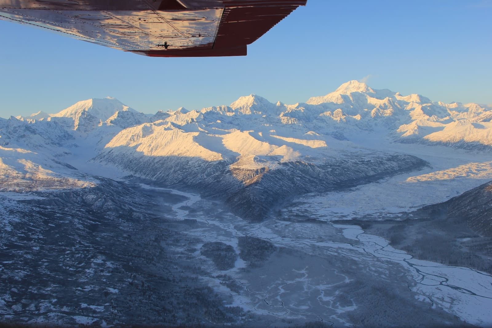 Flightseeing from plane wing over snowy peaks at sunrise