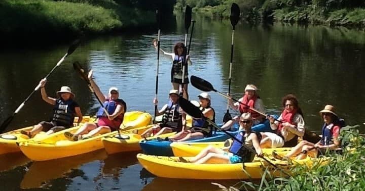 Friends kayaking together on slow river through green woods