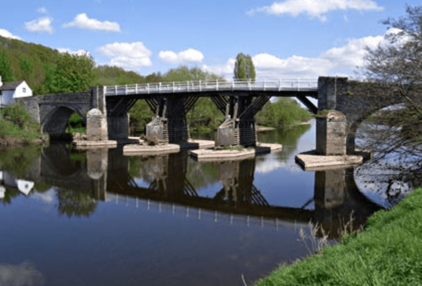 Historic stone bridge reflected over calm river, canoe trips