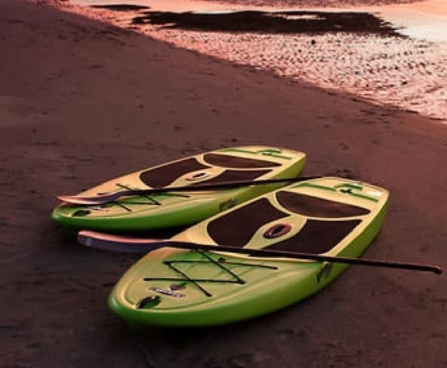 Two paddleboards resting on sandy beach at sunset, calm shore
