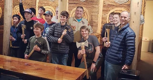 Youth group holding axes inside rustic indoor axe throwing lane