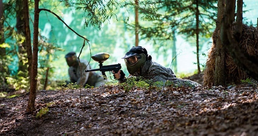 Paintball players firing markers in dense forest terrain