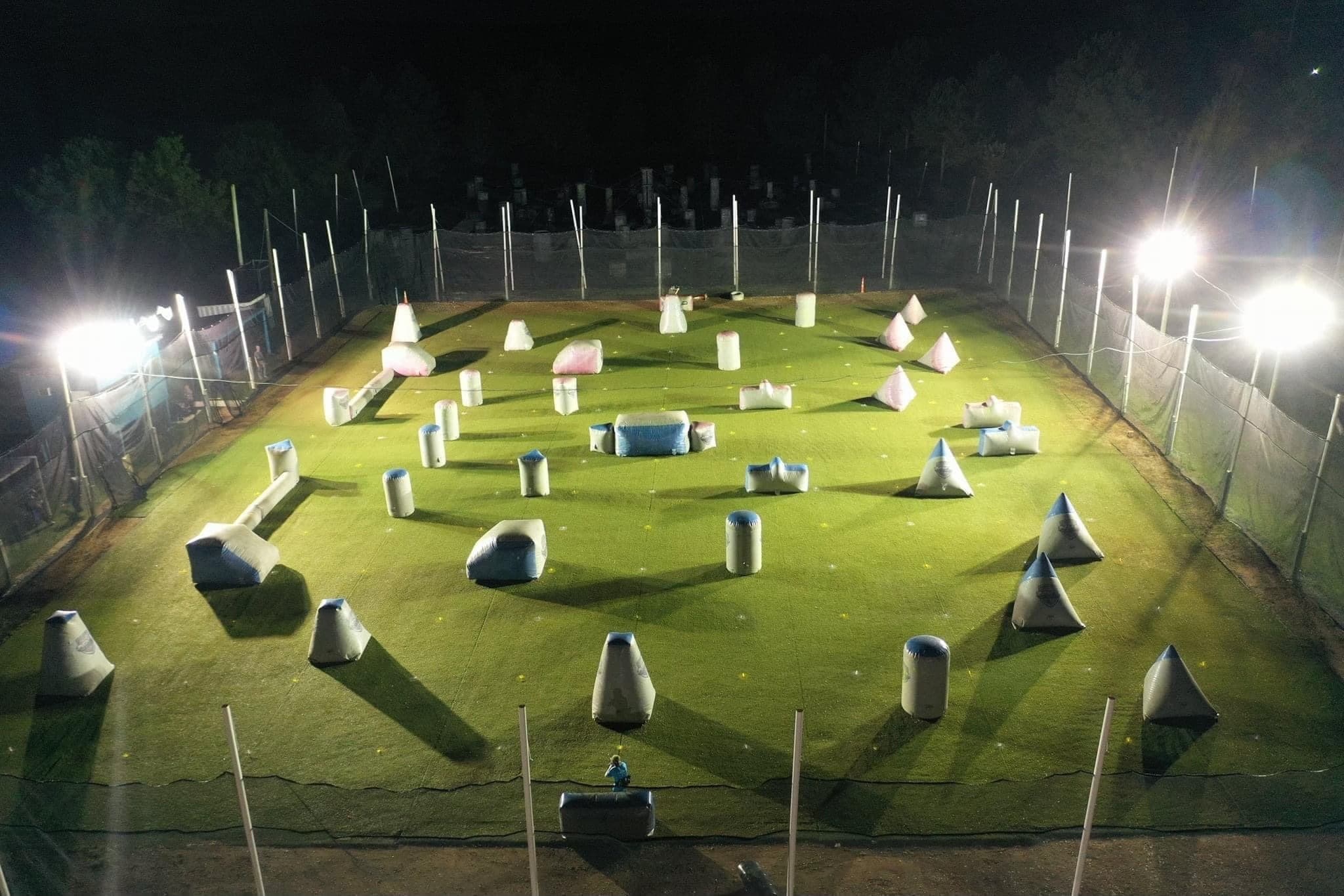 Aerial view of lit paintball field layout at night with bunkers