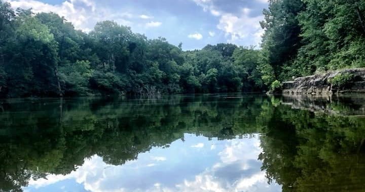 Calm forested river reflecting sky, scenic paddling vista