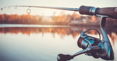 Fishing rod and reel set against calm lake at golden hour