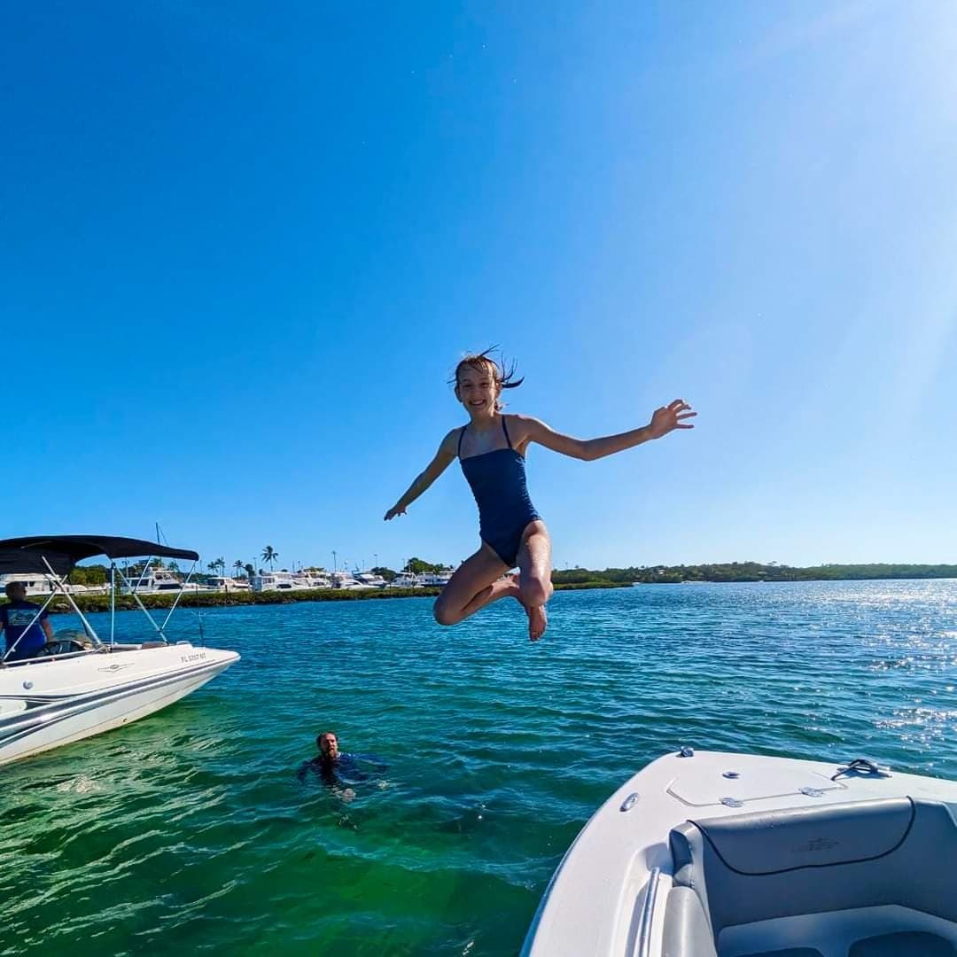 Woman jumping from boat into clear blue coastal bay water