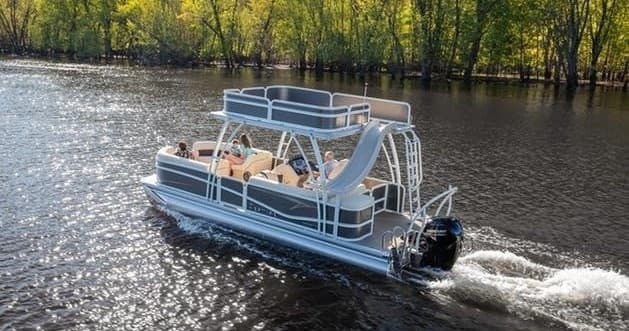 Pontoon boat cruising river with passengers near tree-lined shore