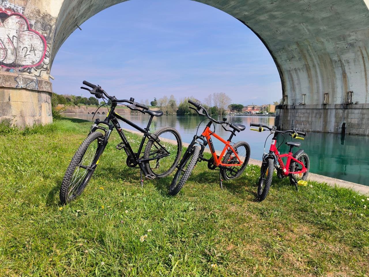 Three touring bikes parked under stone bridge beside river