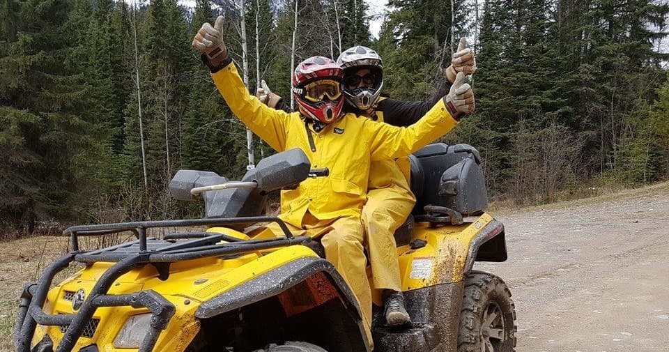 Two riders on yellow ATV celebrating on muddy forest trail