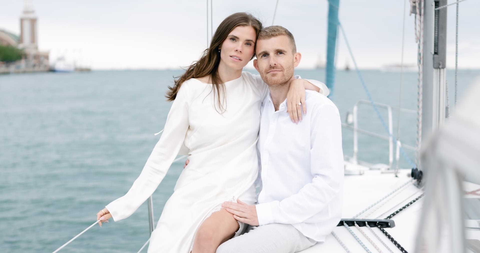Couple on sailboat deck posing with lake and city backdrop
