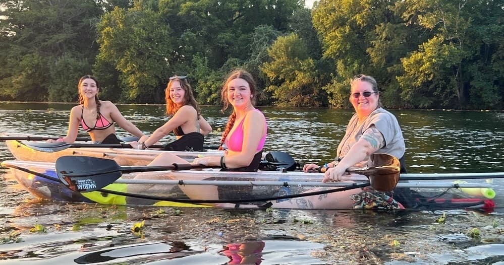 Four paddlers smiling in clear kayaks on calm Austin waterway