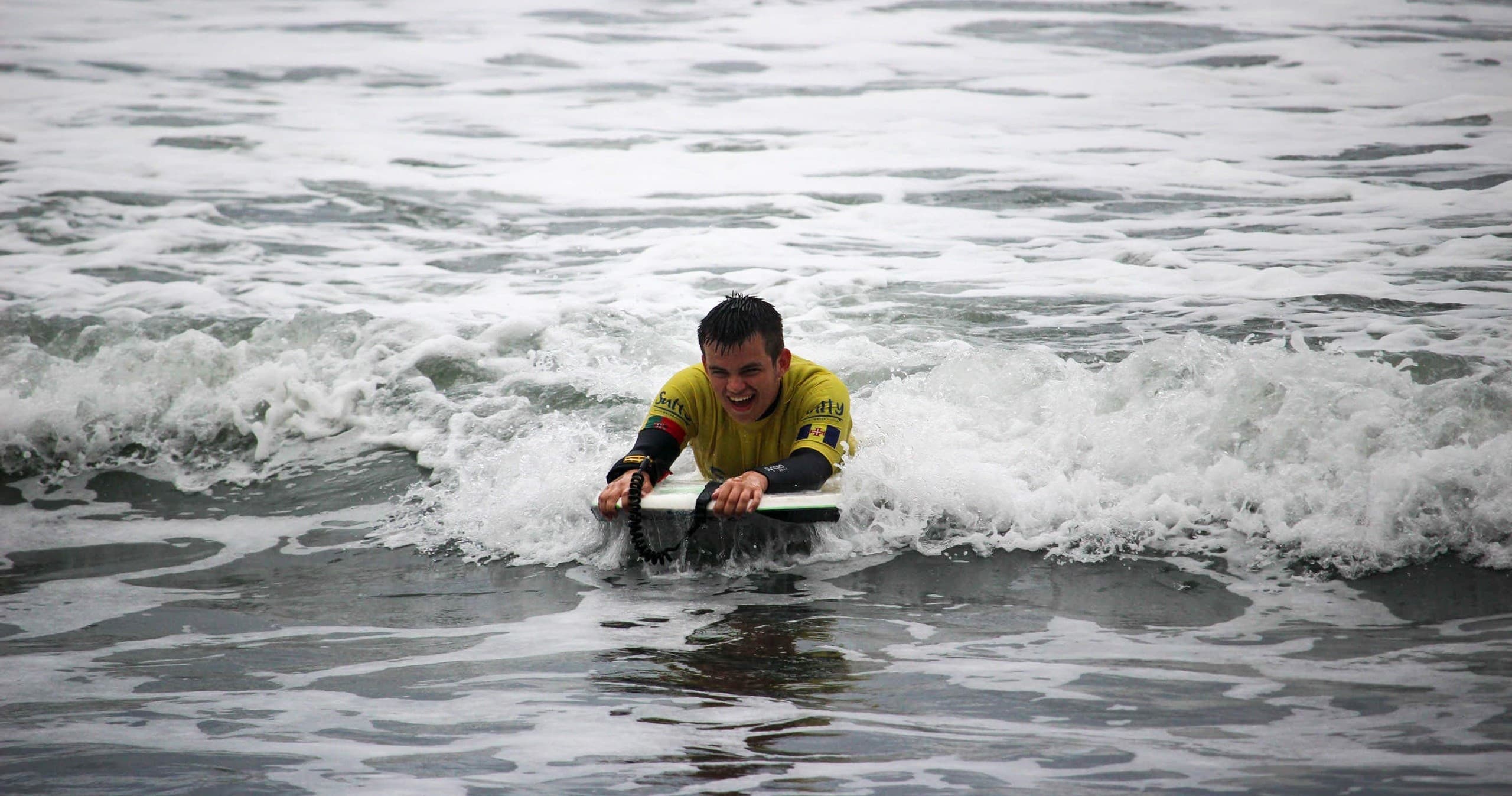 Bodyboarder riding breaking wave near shore in wetsuit