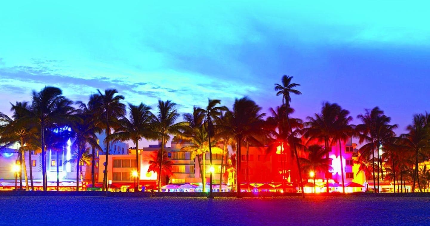 Colorful Miami Beach oceanfront at night with lit palm-line hotels