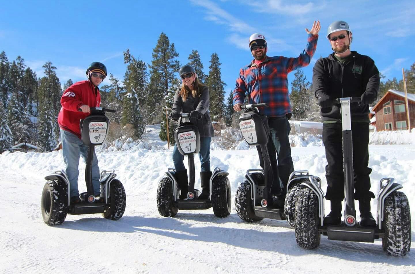 Four people on Segways riding across snowy mountain trail