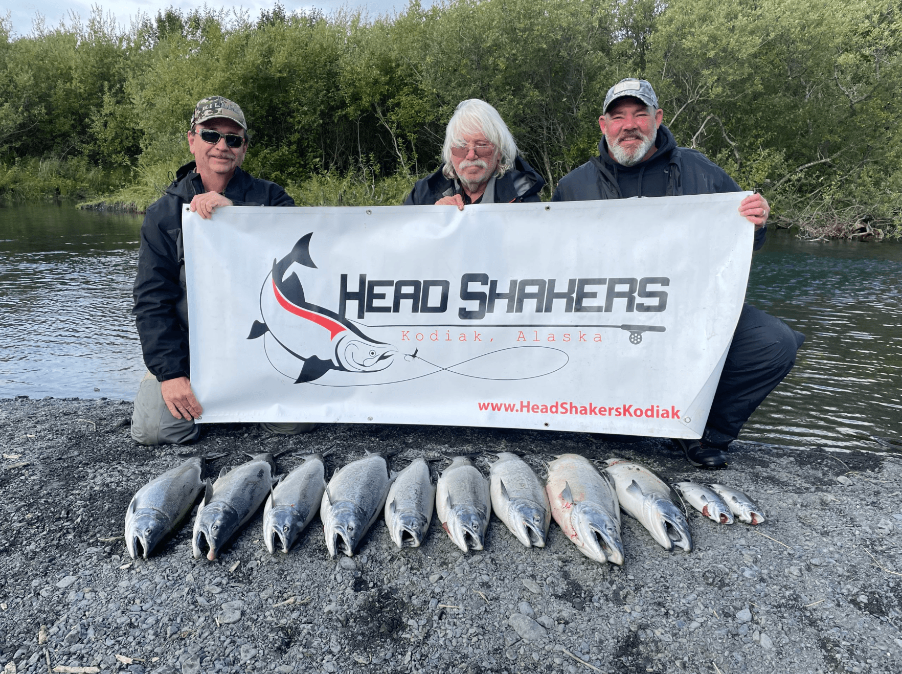 Three anglers posing with lined salmon catch on Kodiak riverbank