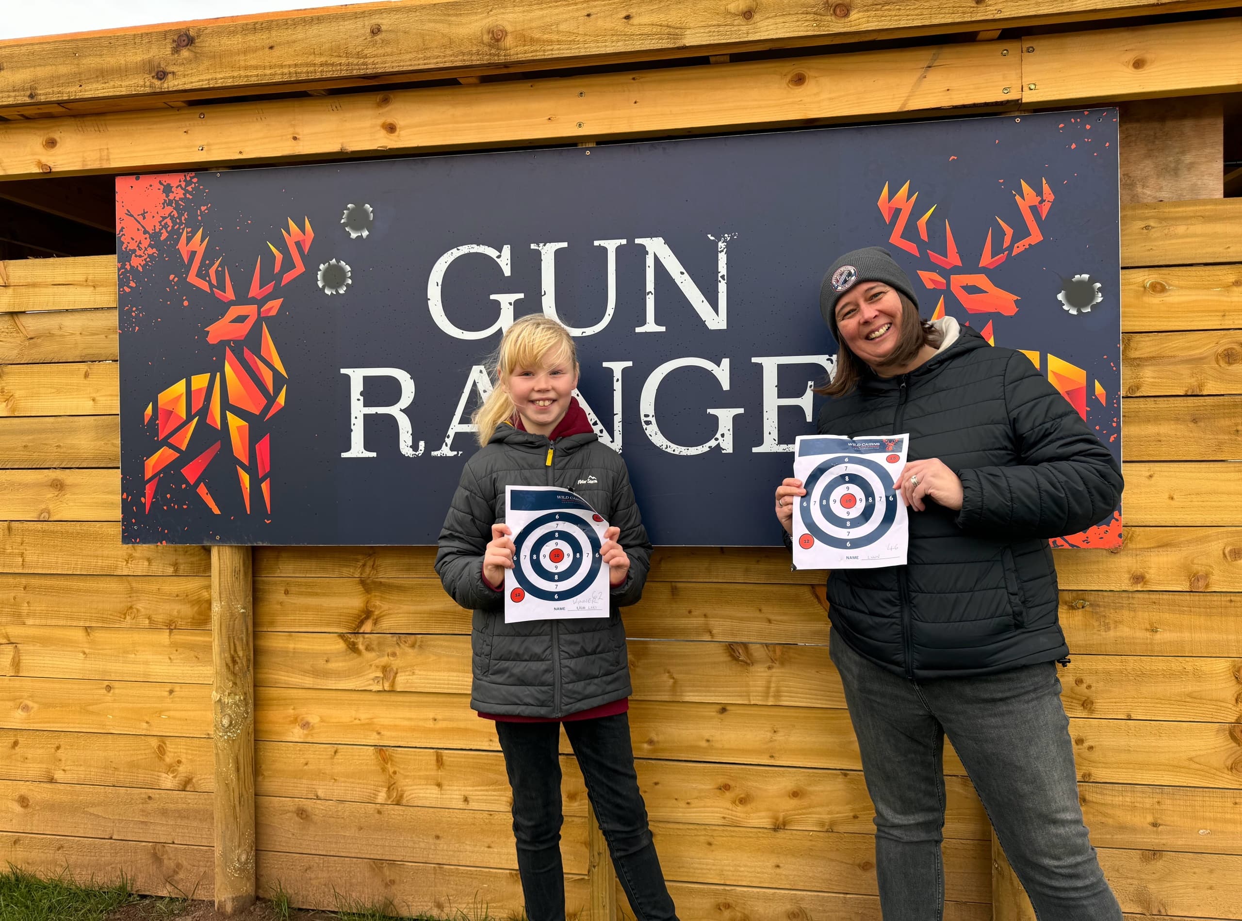Smiling participants holding bullseye targets at outdoor gun range