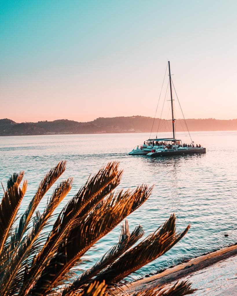 Sailboat at sunset near palm-fringed shore on Tagus River
