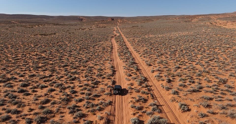 Aerial view of 4x4 vehicle driving desert tracks at sunset