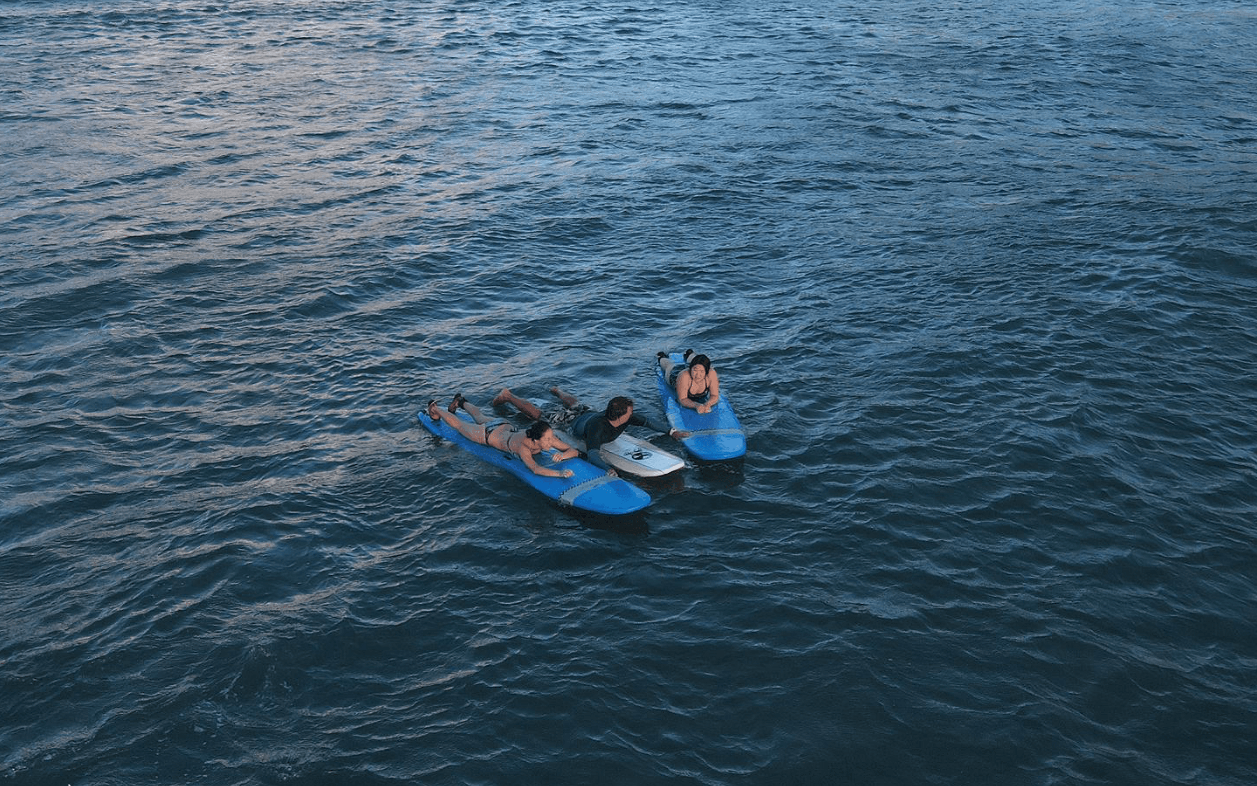 Aerial view of three surfers on boards in open deep blue ocean